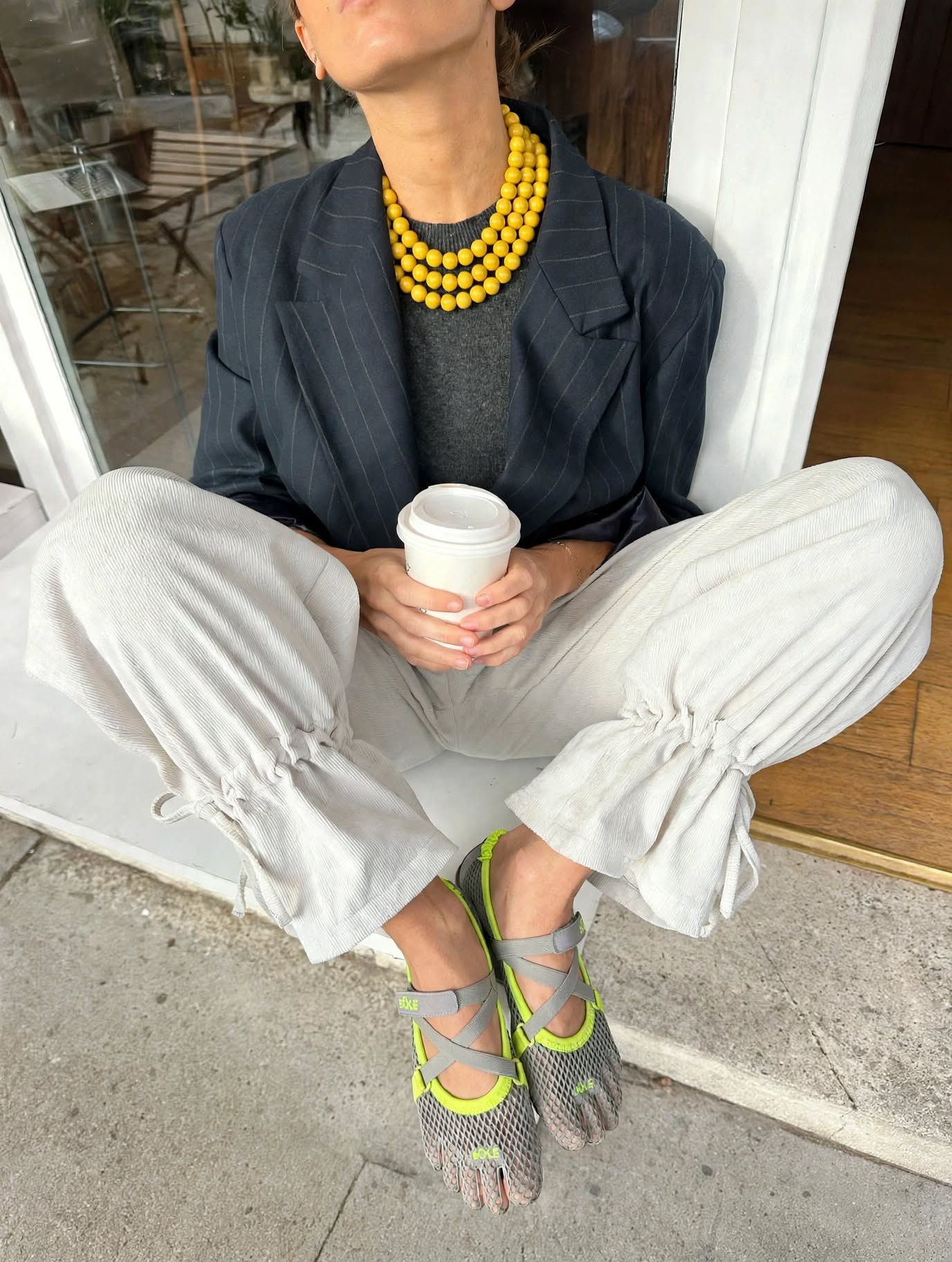 A woman relaxing with coffee in grey Sôle five-toe flats with neon-yellow accents